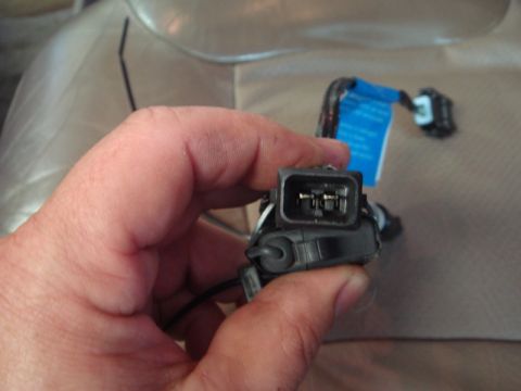 1996 Ford Bronco - A hand holds a car electrical connector with a blue tag attached to the wiring harness.