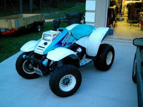 1986 Ford Bronco - This Polaris ATV is parked outside a garage next to a trailer.