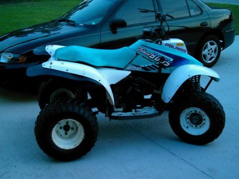 1986 Ford Bronco - A Polaris Trail Boss 250 ATV is parked in front of a black sedan.