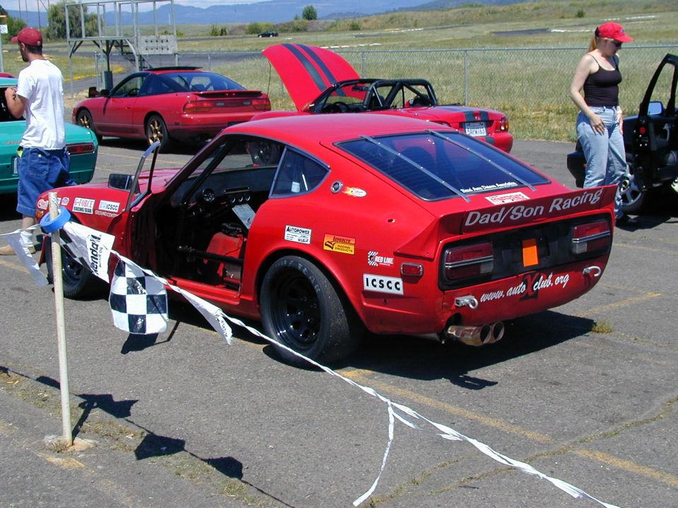 Red Datsun Z race car with Dad/Son Racing decals, rear three-quarter view in a paddock area