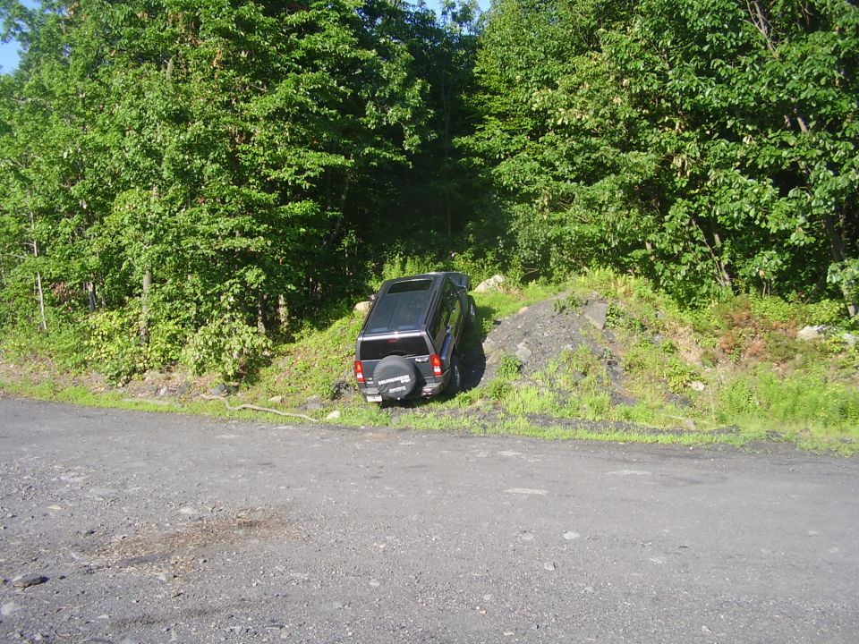 2003 Jeep Wrangler parked on a dirt incline next to trees