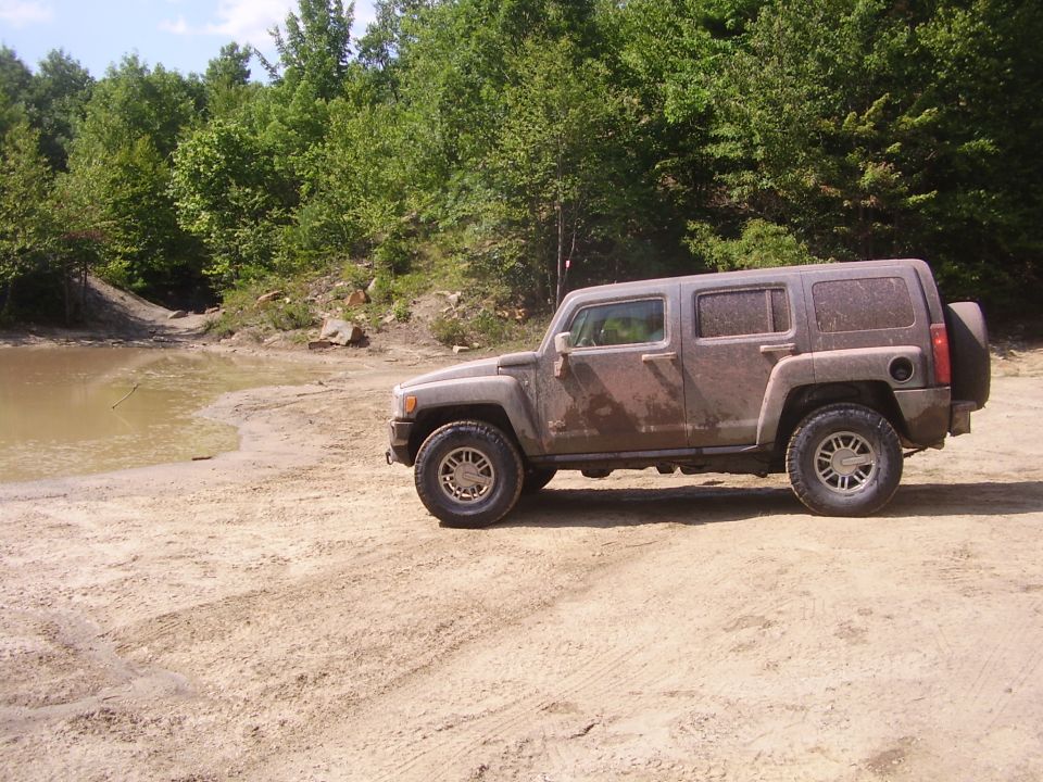 Mud-covered Hummer H3 parked on a dirt track next to a muddy puddle
