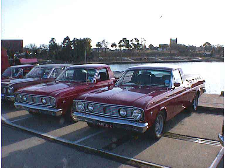 Two dark red Ford Falcon utes parked by water, front and 3q-front views
