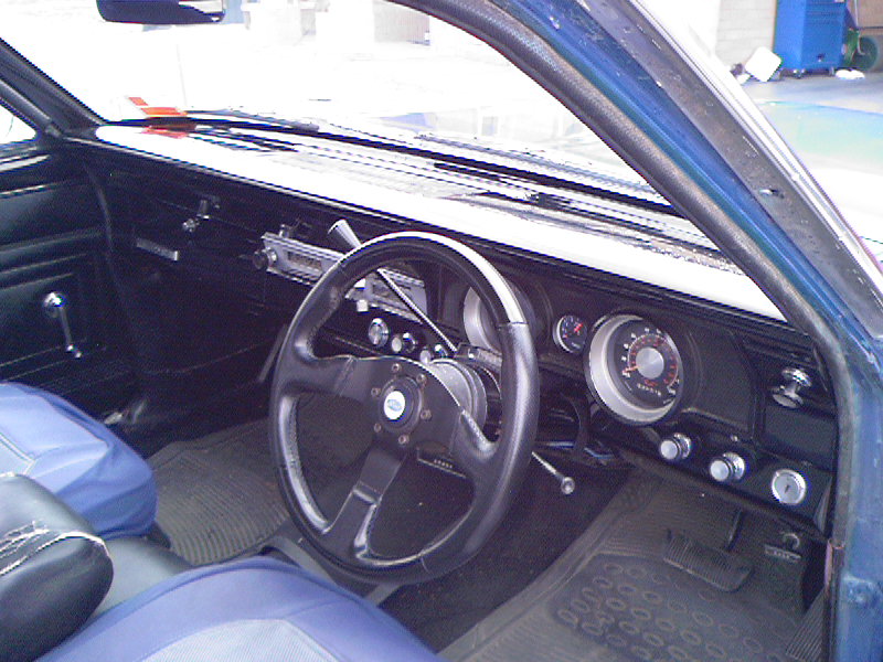 Right-hand-drive interior with blue vinyl seats, black dash, and aftermarket three-spoke steering wheel