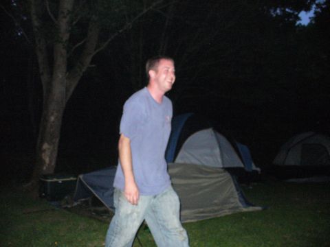 1991 Ford Probe - A man walks past several tents set up in a grassy area at night.