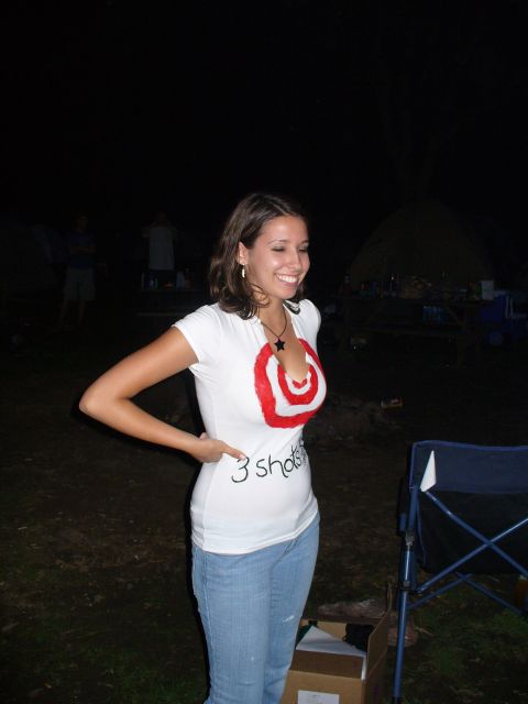1991 Ford Probe - Woman wearing a t-shirt with a target graphic and text, standing outdoors at night with tents in the background.