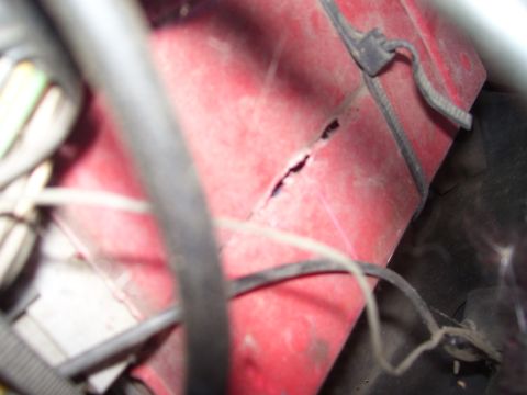 1986 Ford Bronco - A close-up view of a damaged red component within a vehicle's engine bay.