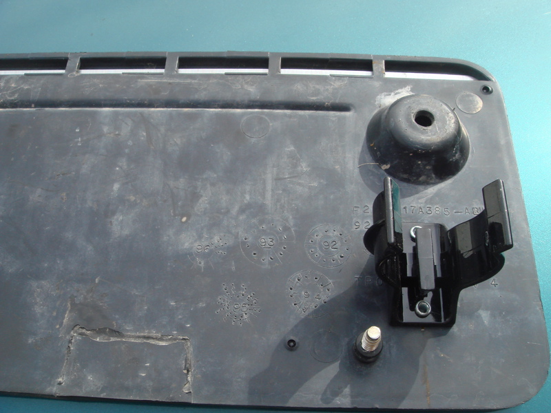 Black plastic trim piece with embossed circular markings, some with numbers like '92' and '93', and a black plastic mounting bracket attached