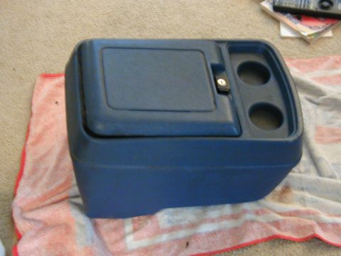 1986 Ford Bronco - This blue plastic center console features a storage compartment and dual cup holders, shown here on a towel.