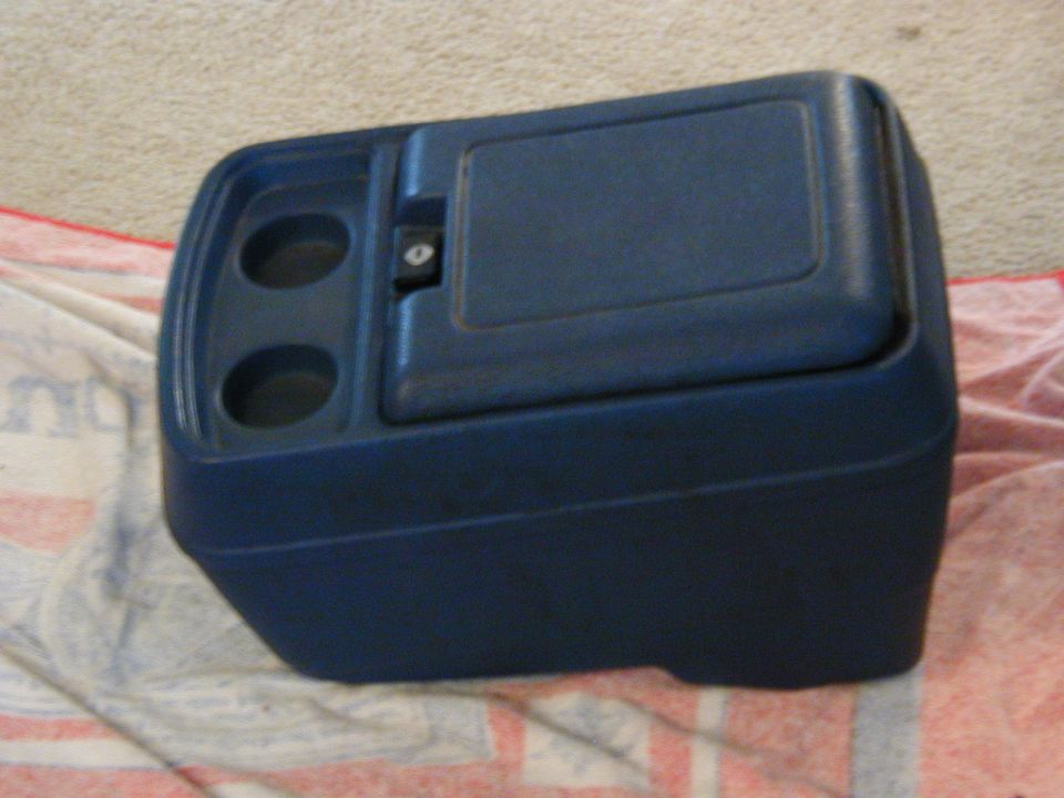Blue plastic center console with two cup holders and a locking storage compartment, resting on a patterned cloth