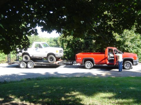 1979 Ford F-250 - A white pickup truck is loaded onto a trailer, which is then towed by a red pickup truck.