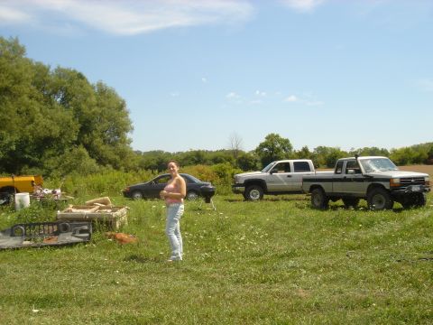 1979 Ford F-250 - A woman stands in a grassy field next to a car and two pickup trucks under a clear blue sky.