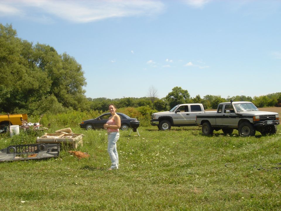 Two pickup trucks and a car in a grassy field with a woman