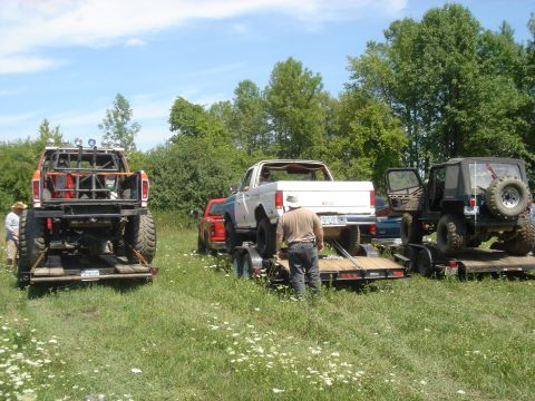 1979 Ford F-250 - Several trucks and a Jeep are parked on trailers in a grassy field on a sunny day.