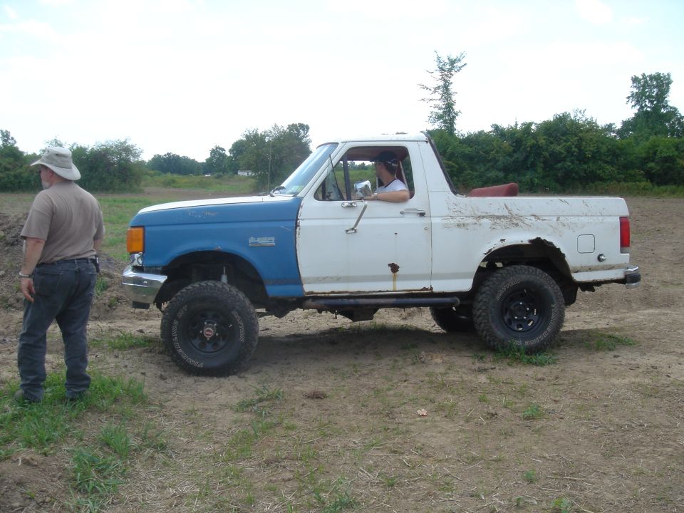 Ford Bronco with blue front fenders and white rear body, lifted on off-road tires
