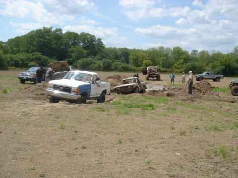 1979 Ford F-250 - A two-tone pickup truck is stuck in a mud pit alongside other vehicles during an off-road event.