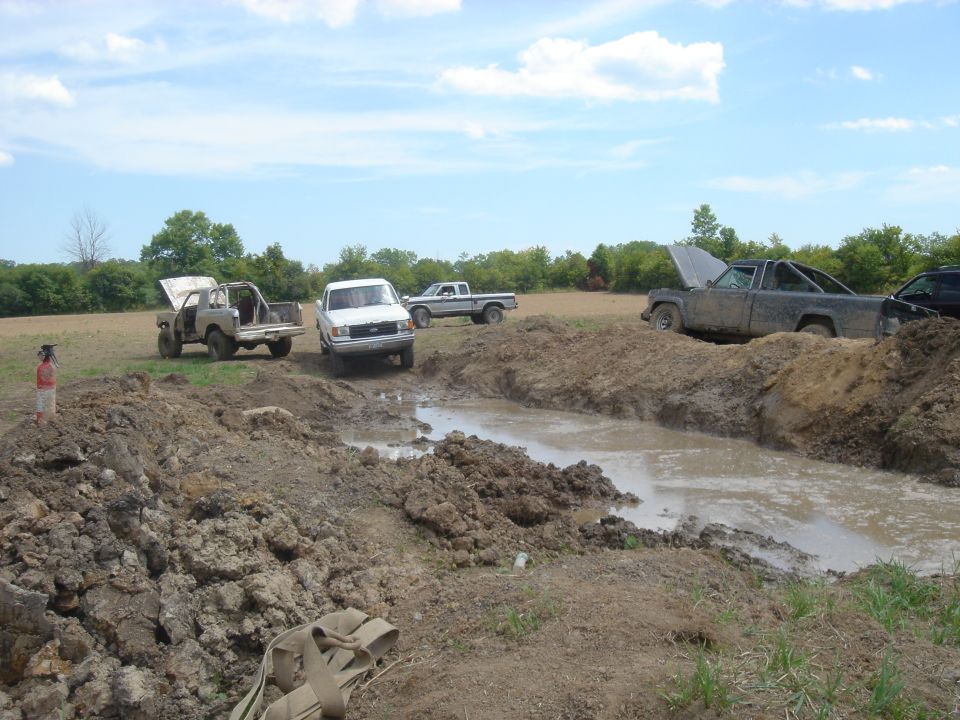 Several trucks are stuck in a muddy off-road course with one person standing nearby