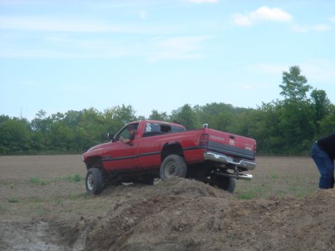 1979 Ford F-250 - A red pickup truck navigates a dirt obstacle under a cloudy sky.