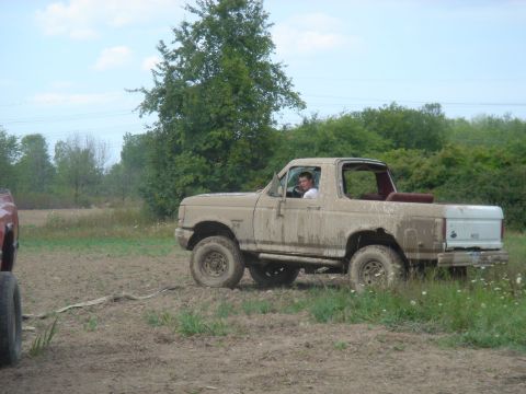 1979 Ford F-250 - A tan 4-door SUV, possibly a Ford Bronco, is driven off-road through muddy terrain with another vehicle partially visible to the left.