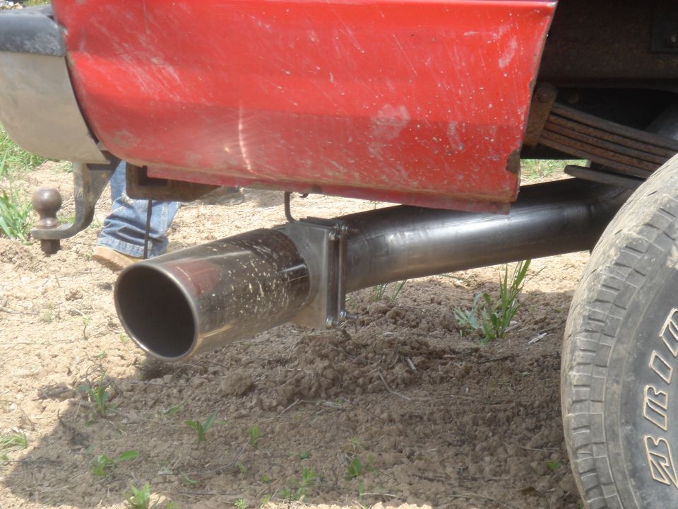 Close-up of a large exhaust pipe exiting from under a red vehicle, showing leaf springs and part of a tire