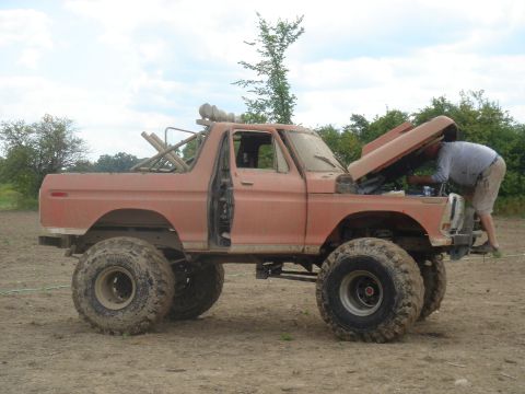 1979 Ford F-250 - A person works on the engine of a heavily modified orange Ford Bronco with oversized tires.