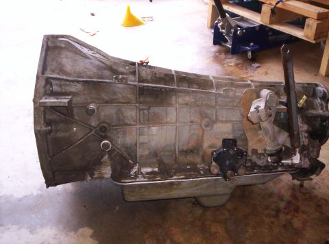 1995 Ford Bronco - A dirty automatic transmission is shown on the floor, possibly removed from a vehicle for repair or replacement.
