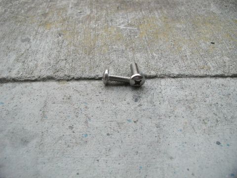 1990 Ford Thunderbird - Two screws are visible on a concrete surface, with one slightly overlapping the other.
