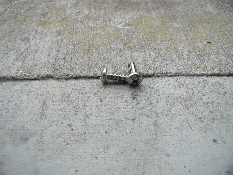 Two stainless pan-head Phillips machine screws on a concrete floor