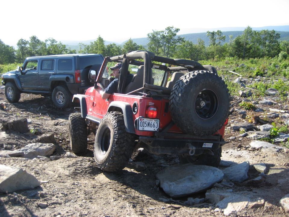 Red Jeep Wrangler on rocky terrain, rear view. License plate 005M663. Another SUV is behind it