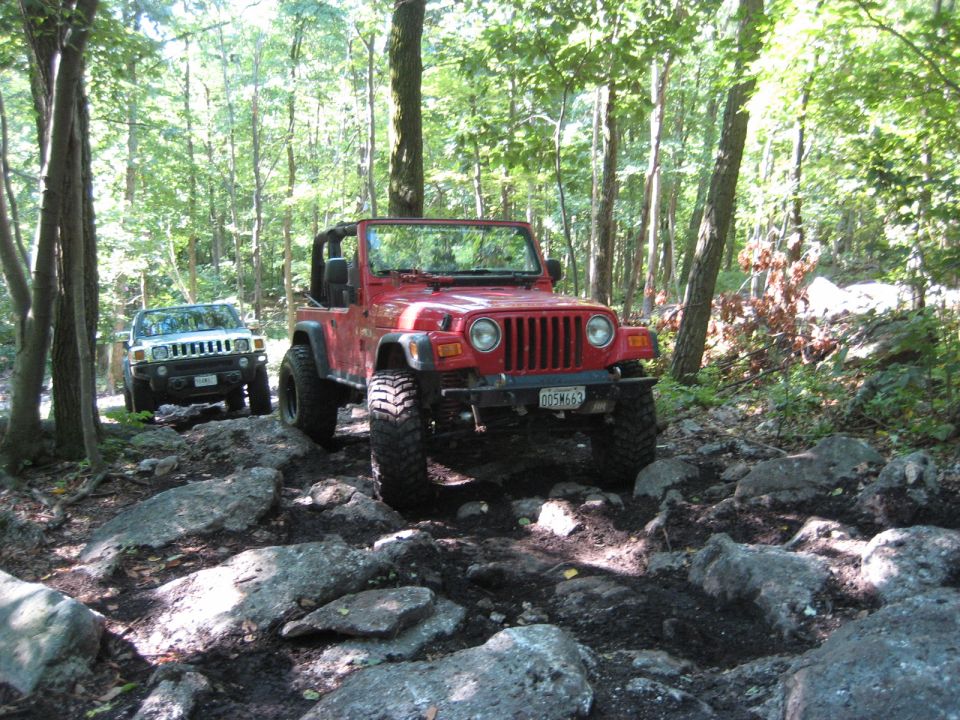 Red 2003 Jeep Wrangler navigating a rocky forest trail with a white Hummer behind it