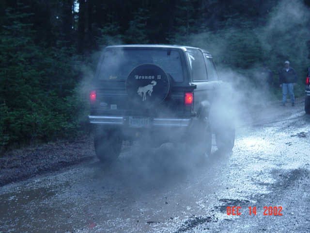 Rear of a Ford Bronco II with spare-tire cover, brake lights on, in heavy steam or dust
