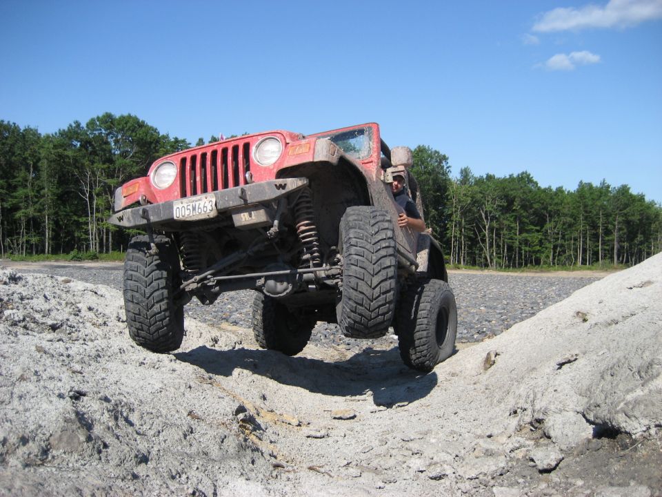 Red 2003 Jeep Wrangler TJ with large tires on a dirt trail, front passenger wheel lifted