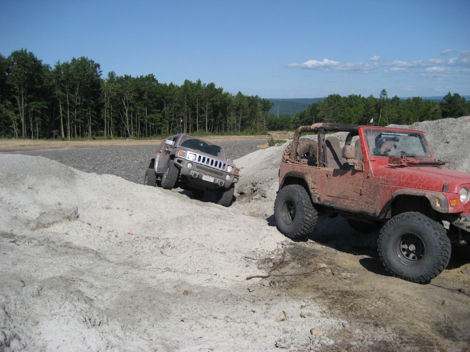 Red Jeep Wrangler and grey Hummer H2 on a dirt trail
