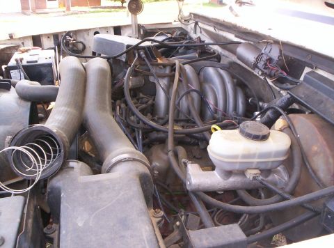 1995 Ford Bronco - Overhead view into the open engine bay of a white Ford truck with the radiator hoses disconnected and laid over the core support, exposing…