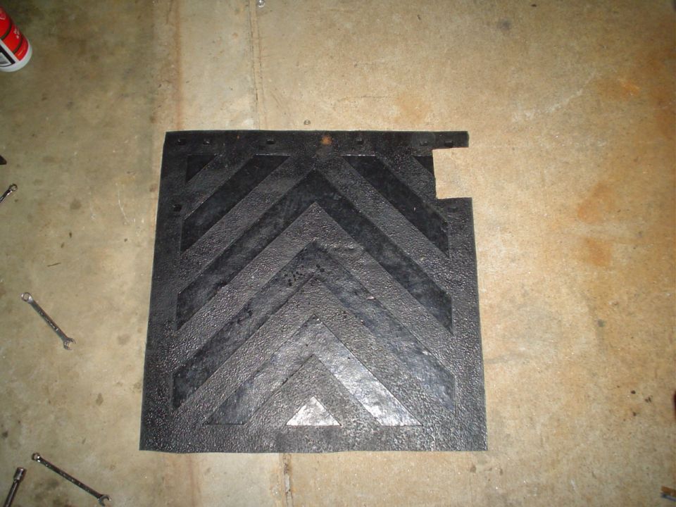 Black rubber mud flap with raised chevron pattern, lying on a concrete floor