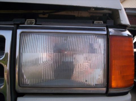 1995 Ford Bronco - Close-up of the driver-side rectangular sealed-beam headlight and amber corner marker lamp on a white Ford truck, with the hood raised abov…