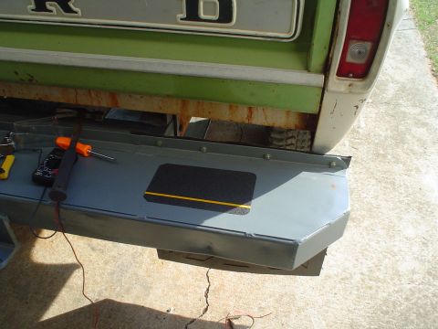 1967 Ford F-250 - A green and white truck's rear end is shown with a new bumper being installed, revealing "FORD" lettering on the tailgate.