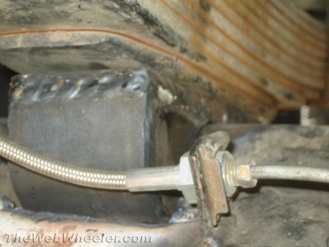 1990 Ford Bronco - Underbody close-up of a fabricated welded steel spring mount with a rusty leaf spring and braided brake line.