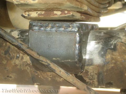 1990 Ford Bronco - Close-up of a freshly welded steel bracket fabricated over an axle tube and leaf spring on a vehicle chassis.