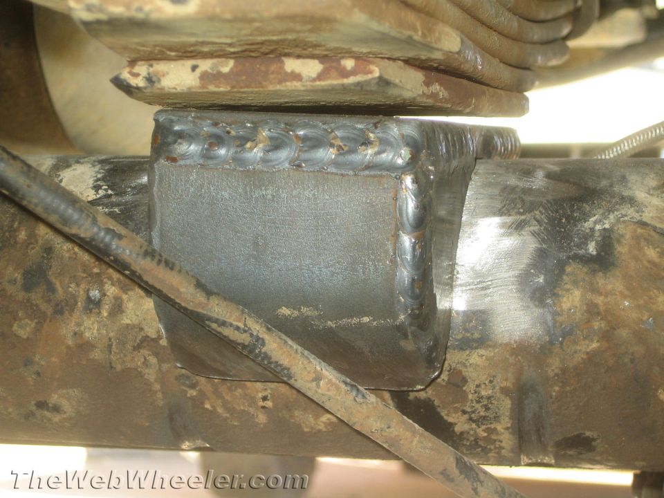 Welded steel bracket clamped over a leaf spring on a vehicle axle tube