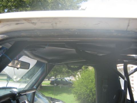 1986 Ford Bronco - The interior of the vehicle shows a prominent roll cage structure, with a view of the outside through the windshield.