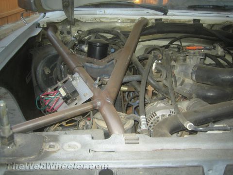 1990 Ford Bronco - Engine bay of a project vehicle with a welded tubular brace, alternator, radiator hoses and wiring, hood removed.