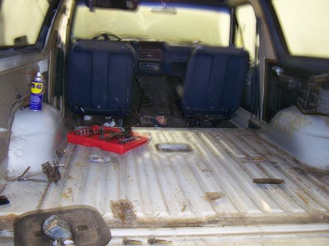 1986 Ford Bronco - The interior of a vehicle shows signs of disassembly, with tools and a can of lubricant present.