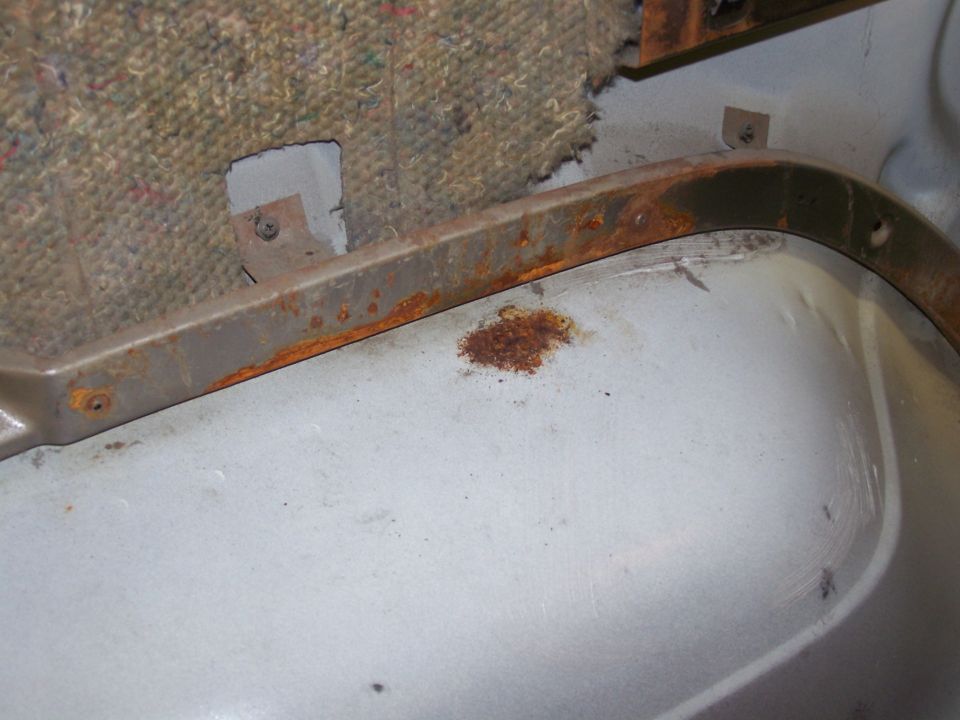 rusted metal trim above light gray floor panel with torn carpet backing
