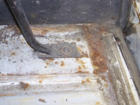 1986 Ford Bronco - The interior floor pan shows significant rust and a bent metal bracket.