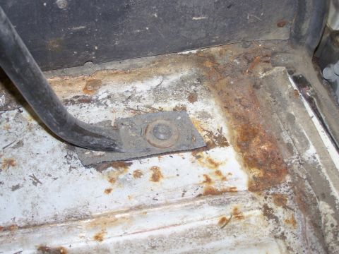 1986 Ford Bronco - Close-up of a rusted floor pan showing a mounting bracket and bolt, likely from a vehicle interior.