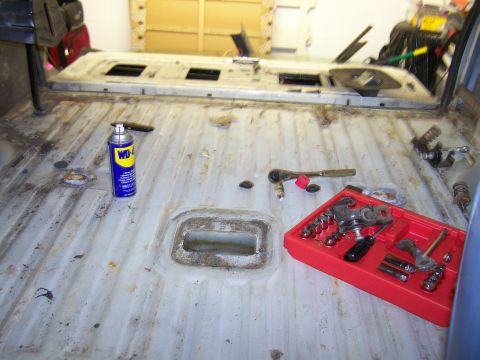 1986 Ford Bronco - Tools and a can of lubricant are on the bare metal floor of a vehicle's interior.