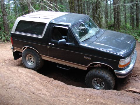 1996 Ford Bronco - This Ford Bronco is navigating a challenging off-road trail, with its tires deep in the dirt.