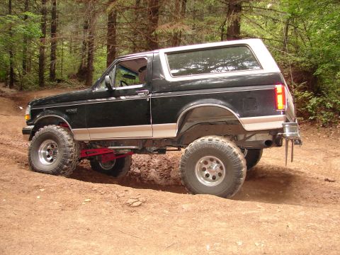 1996 Ford Bronco - A lifted 1996 Ford Bronco navigates a muddy forest path.