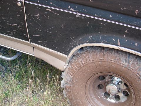 1996 Ford Bronco - A muddy 1992 Ford Bronco is shown from the side, with dirt covering its dark green paint and tires.